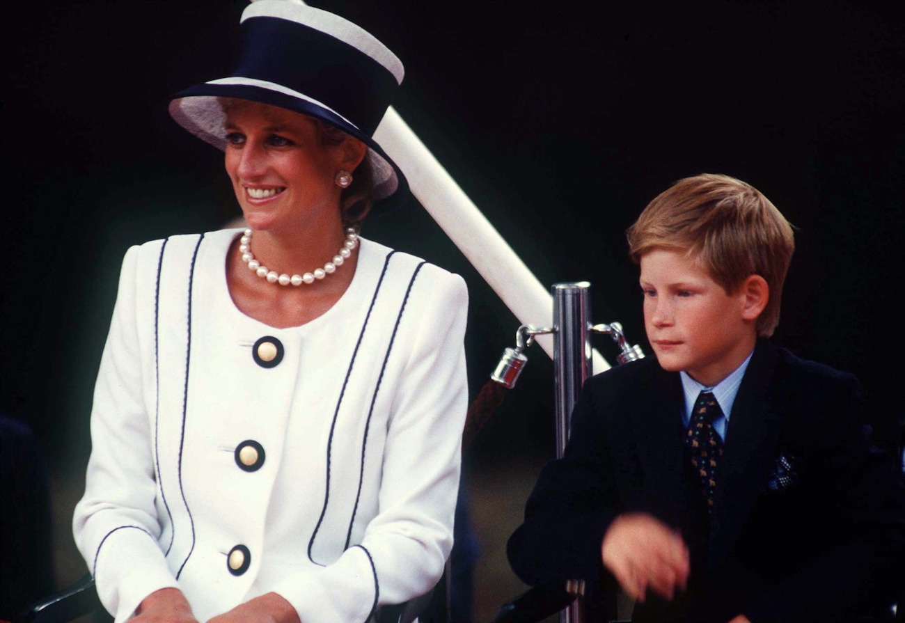 Princess Diana wearing a white outfit and sitting next to young Prince Harry, who is wearing a black suit