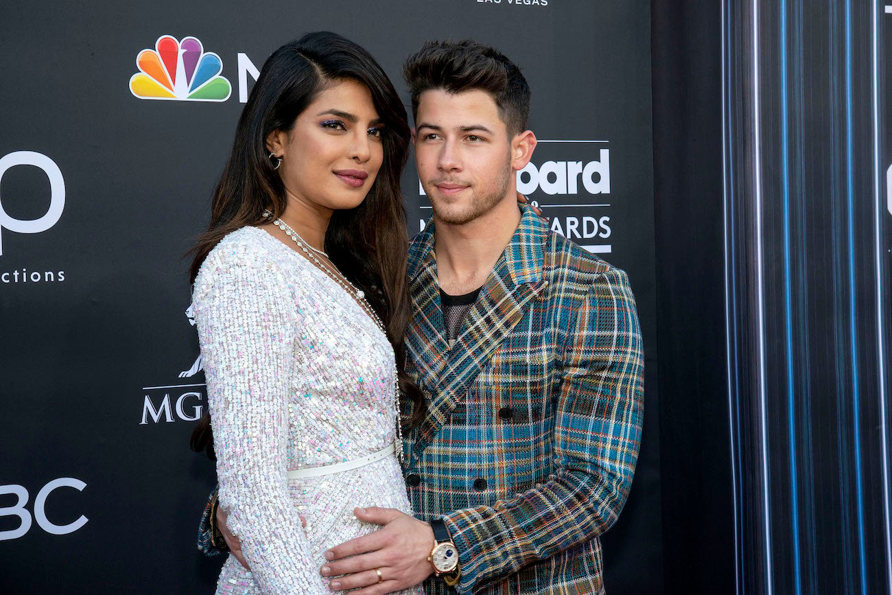 Priyanka Chopra wearing an off-white outfit and standing next to Nick Jonas, who is wearing a plaid jacket