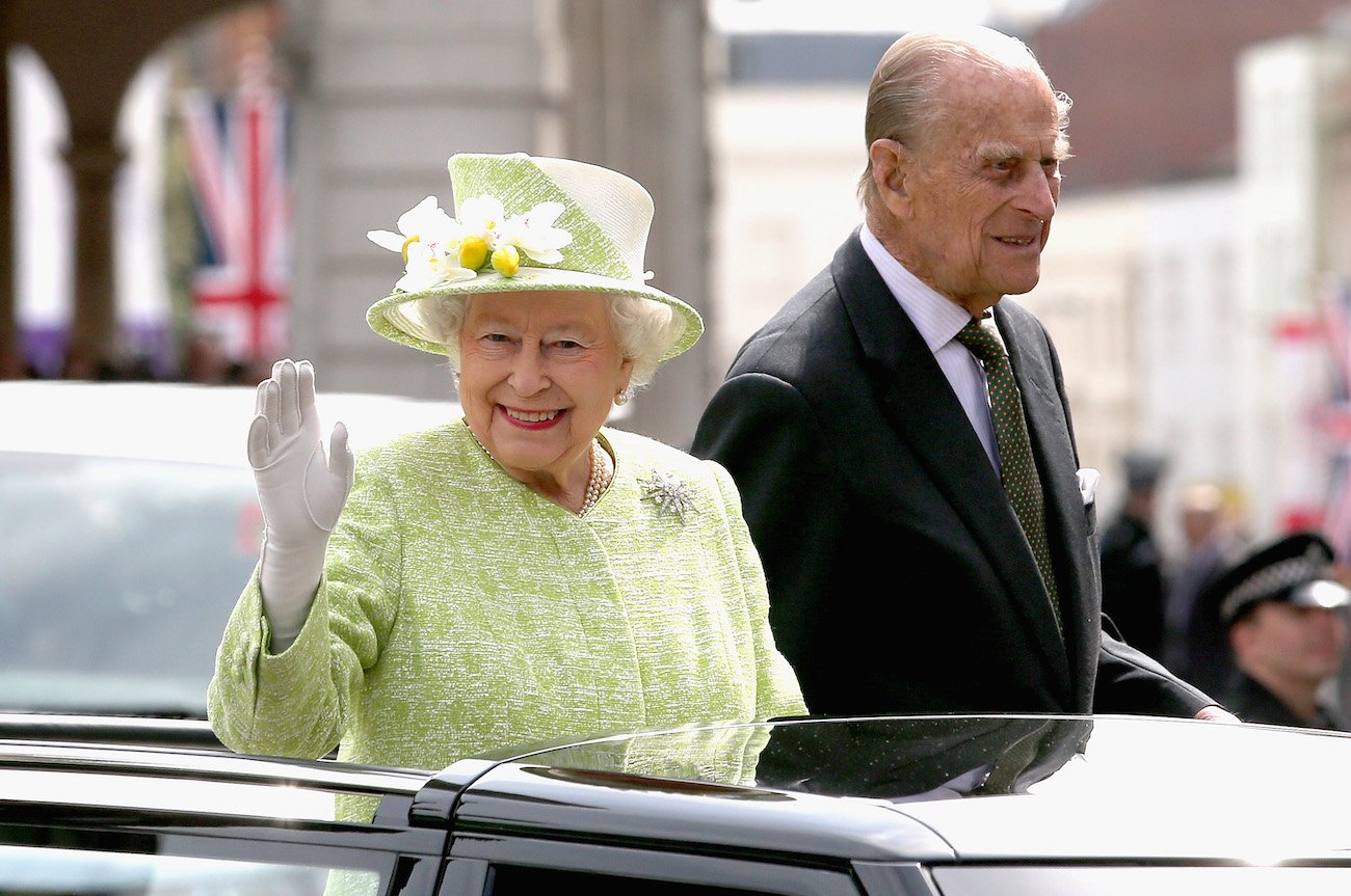 Queen Elizabeth wearing a green outfit and waving while standing next to Prince Philip