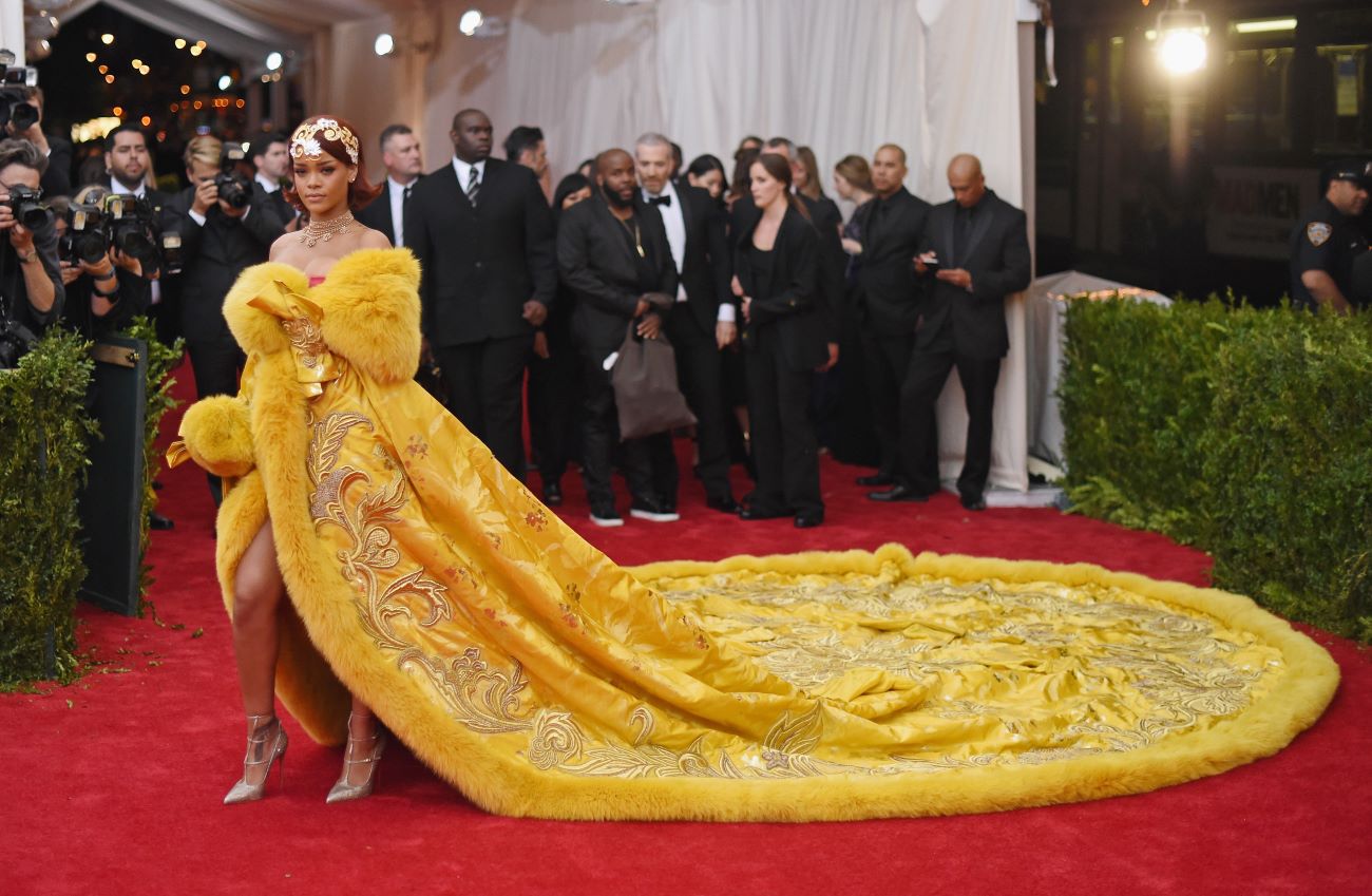 Rihanna wears a yellow dress with a long train on the Met Gala red carpet. 