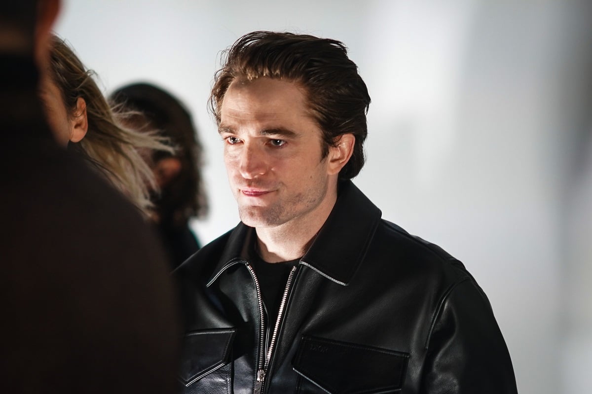 Robert Pattinson posing while wearing a black t-shirt and jacket.