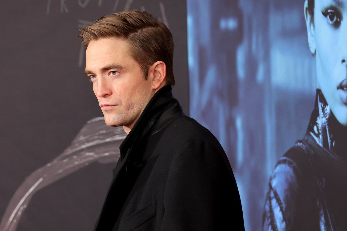 Robert Pattinson posing while wearing a black trench coat.