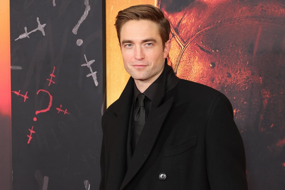Robert Pattinson smirking while wearing a black suit.