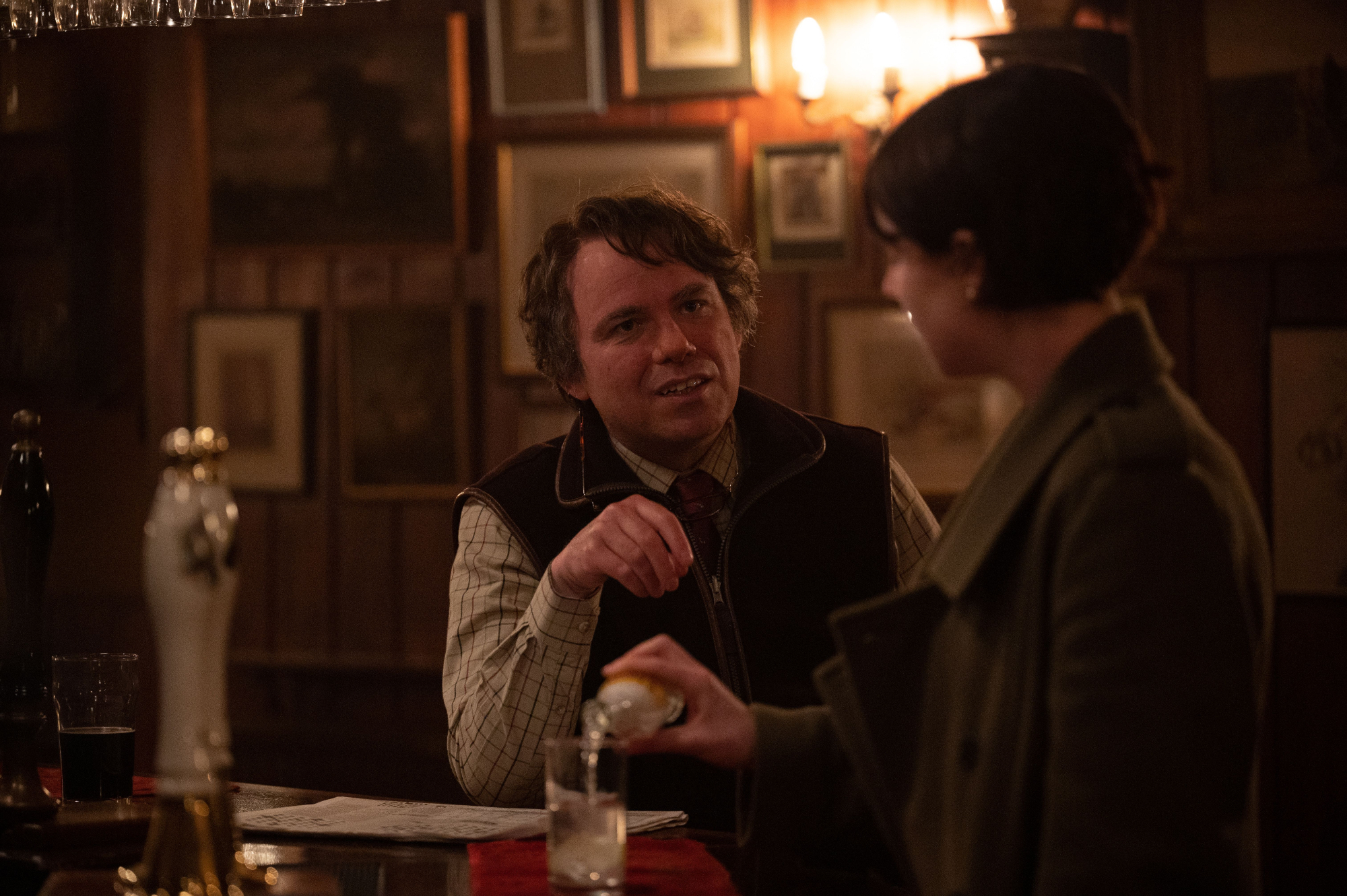 Rory Kinnear as Geoffrey and Jessie Buckley as Harper in 'Men' sitting at the bar in a pub looking at each other