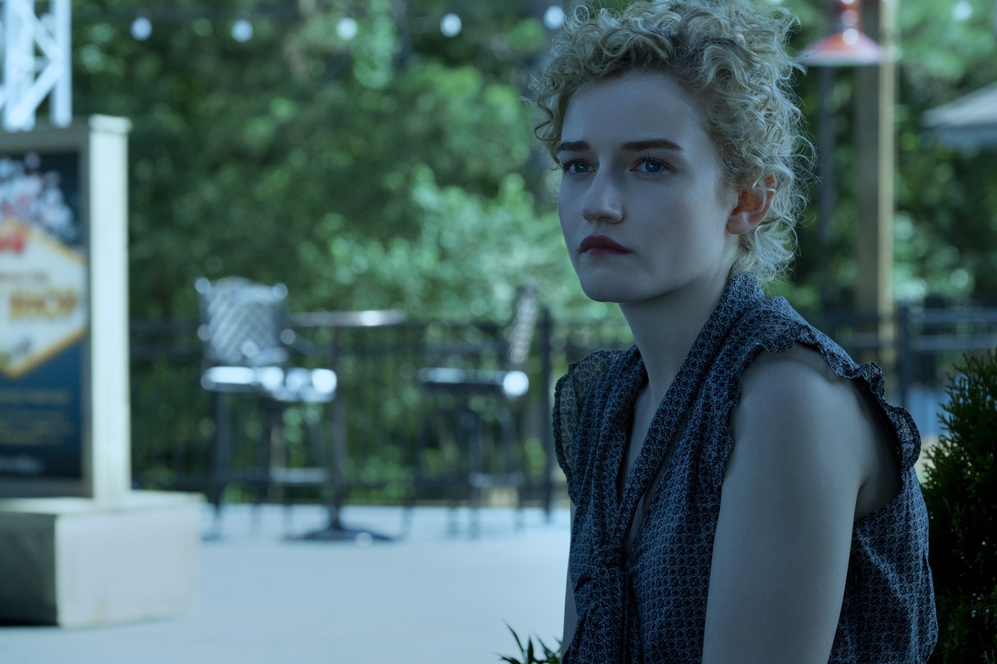 Julia Garner as Ruth Langmore in 'Ozark' Season 3. She's sitting on a bench and staring at something off-screen. There are trees behind her.