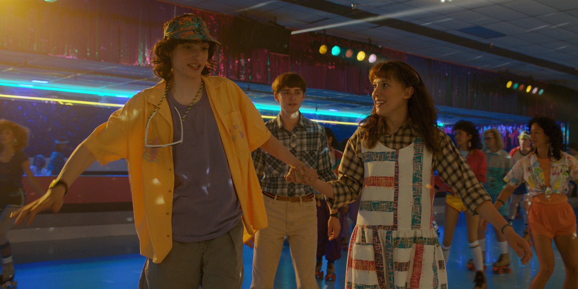 Mike (Finn Wolfhard) holds Eleven's (Millie Bobby Brown) hand rollerskating as Will (Noah Schnapp) looks on behind them in 'Stranger Things' Season 4