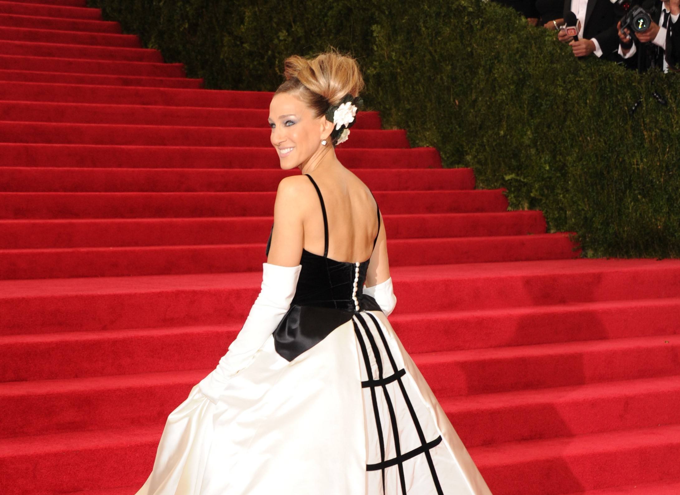 Sarah Jessica Parker wears a black and white gown with white gloves on the Met Gala steps.