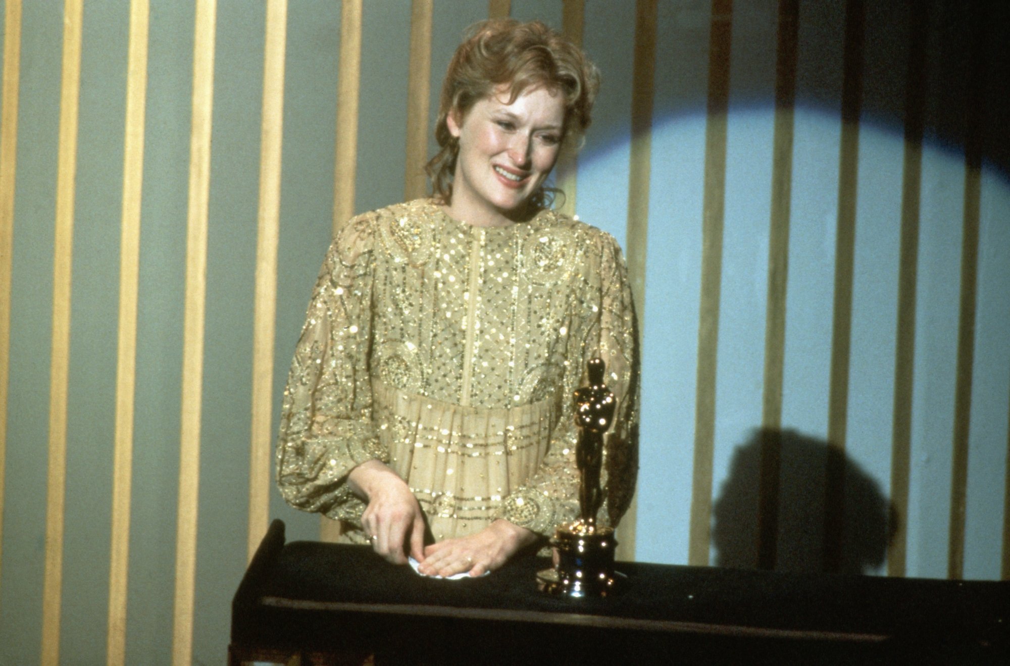 'Sophie's Choice' actor Meryl Streep wearing a gold dress, smiling, with her Oscar statue in front of her