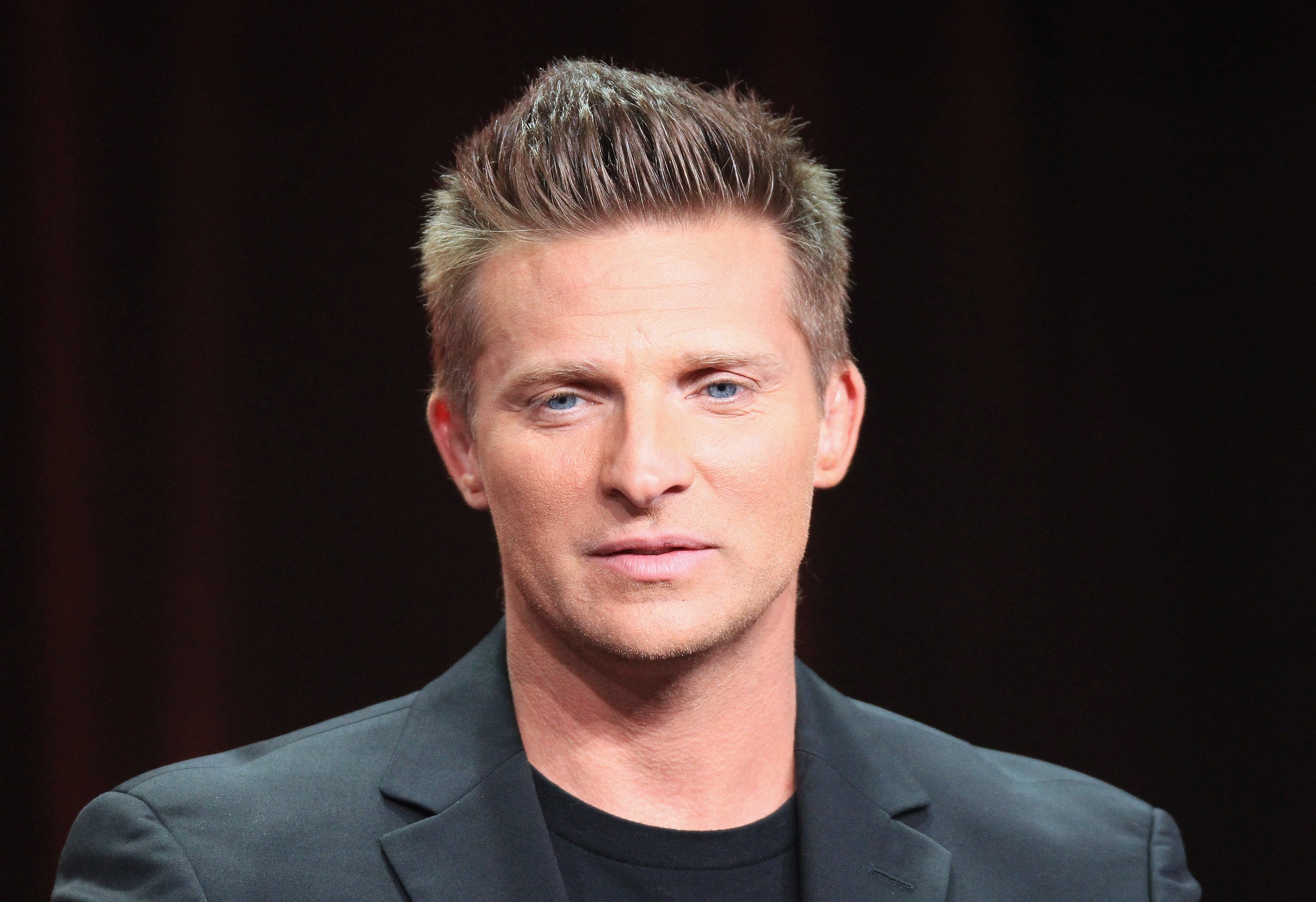 'Days of Our Lives; Beyond Salem' actor Steve Burton wearing a black suit and sitting in front of a black backdrop.