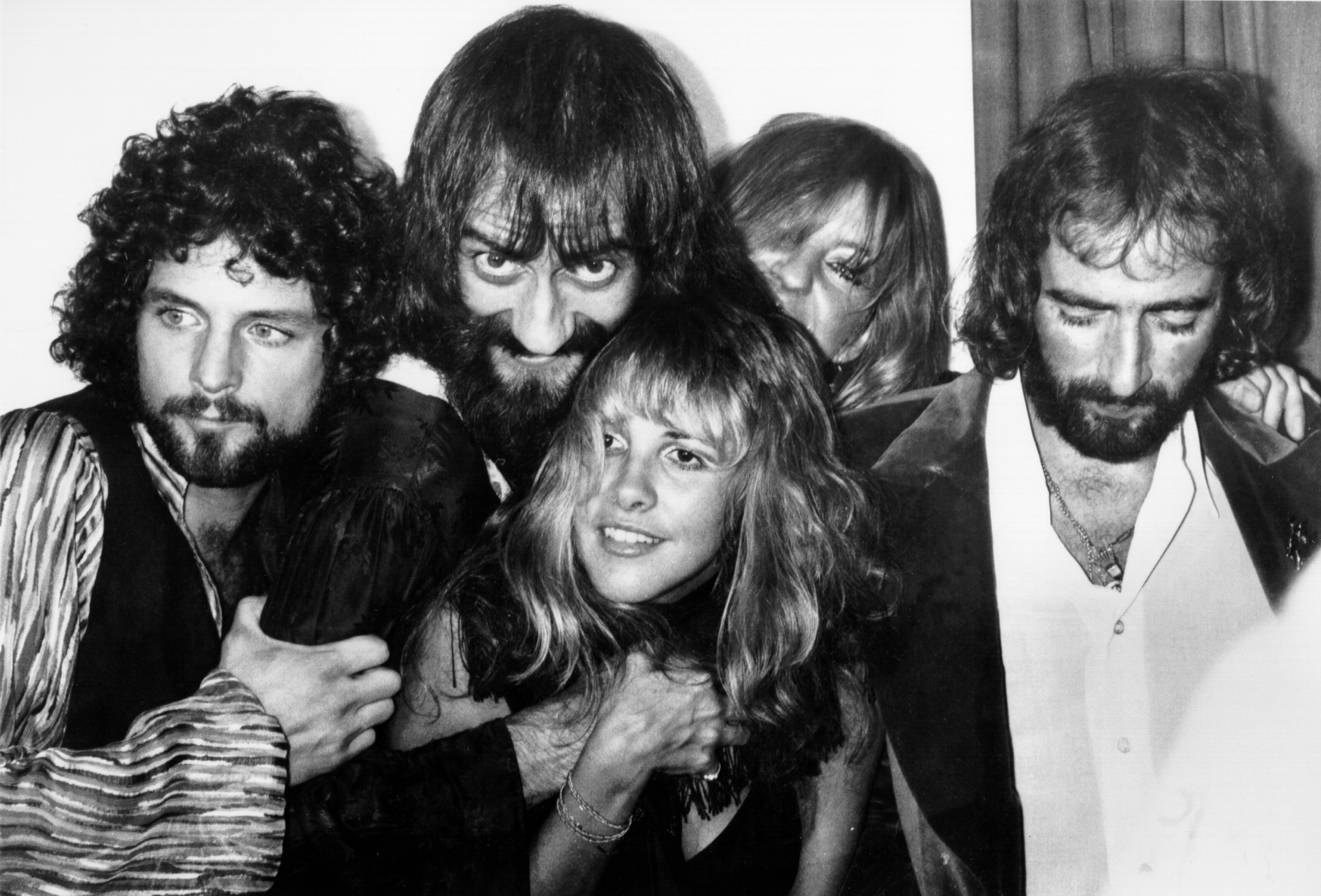 A black and white picture of Fleetwood Mac's Lindsey Buckingham, Mick Fleetwood, Stevie Nicks, Christine McVie, and John McVie posing close together.