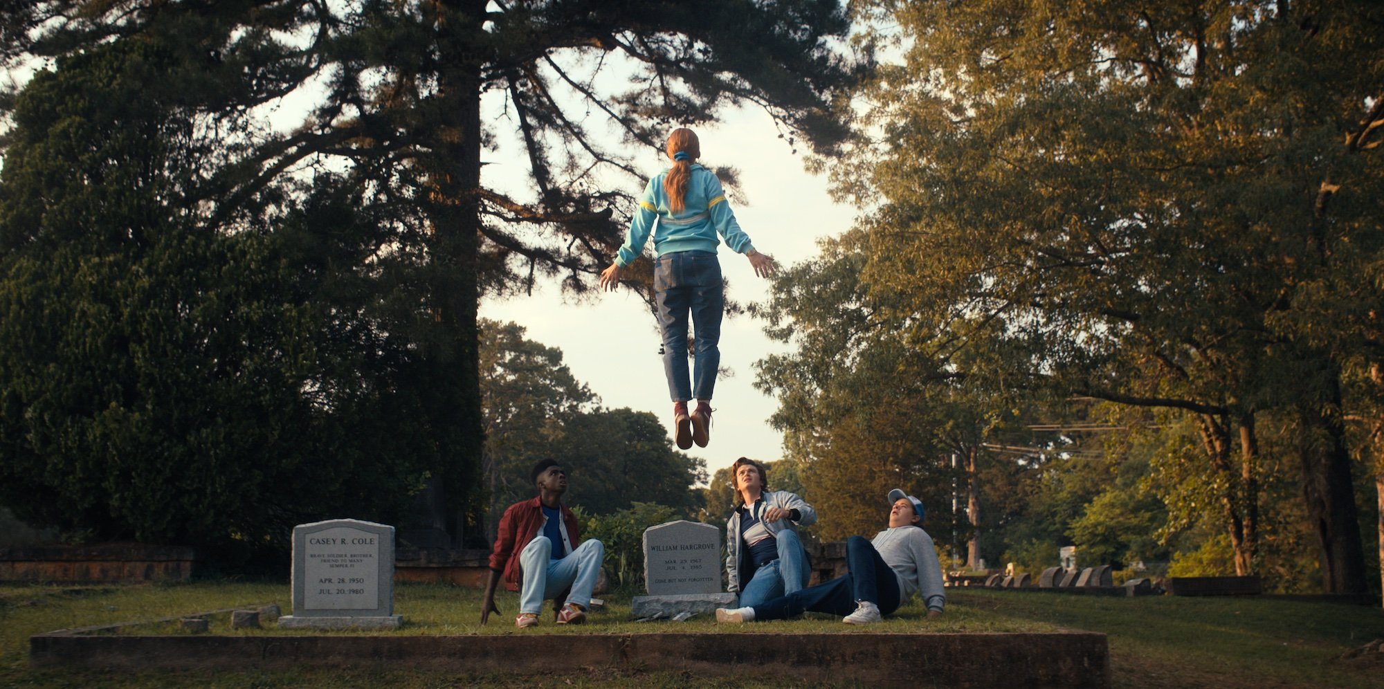Dear Billy features Max levitating in front of Dustin, Steve, and Lucas at Billy's grave in this production still.