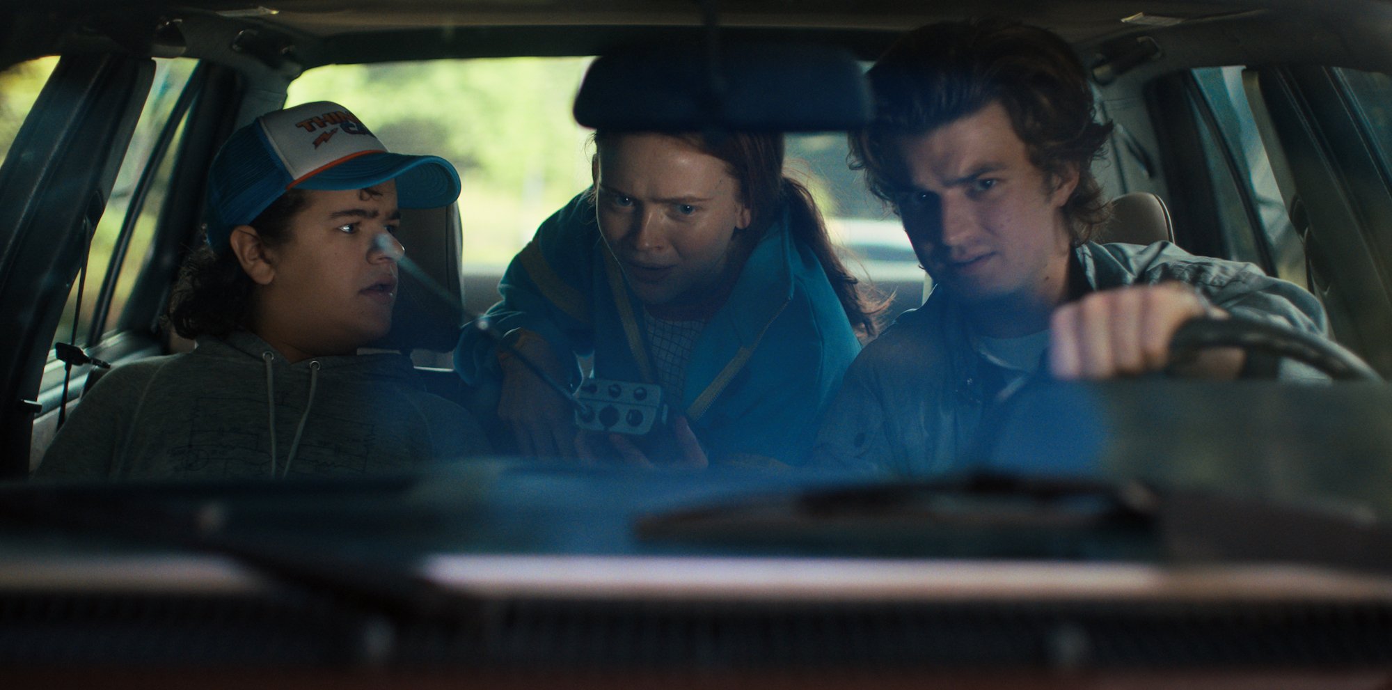 Gaten Matarazzo, Sadie Sink, and Joe Keery sit in a car in a production still from 'Stranger Things' Season 4. What time will Netflix release the new episodes?