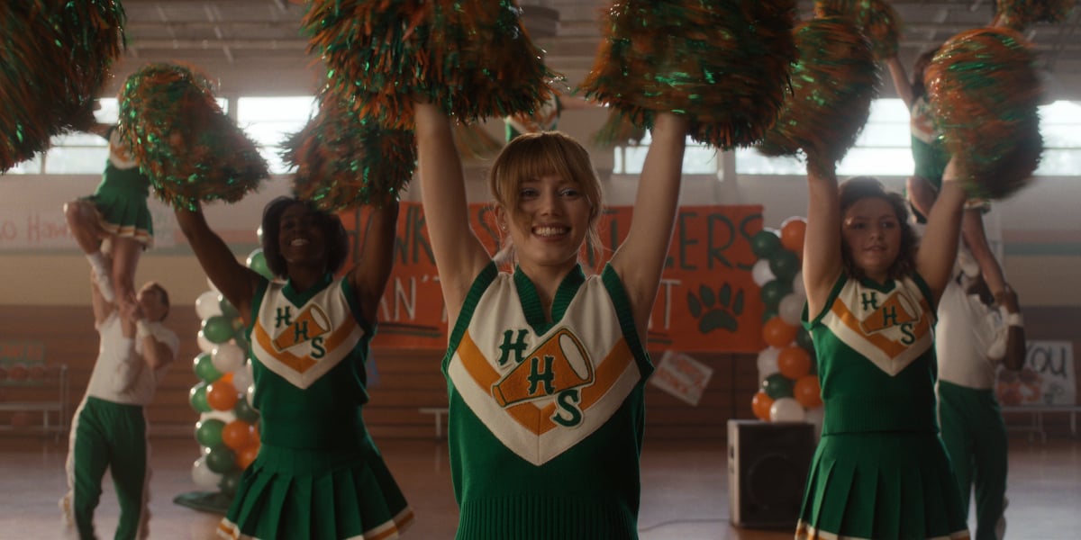 Grace Van Dien als Chrissy in Staffel 4 von „Stranger Things“. Chrissy trägt ein Cheerleader-Outfit und winkt mit Bommeln. 