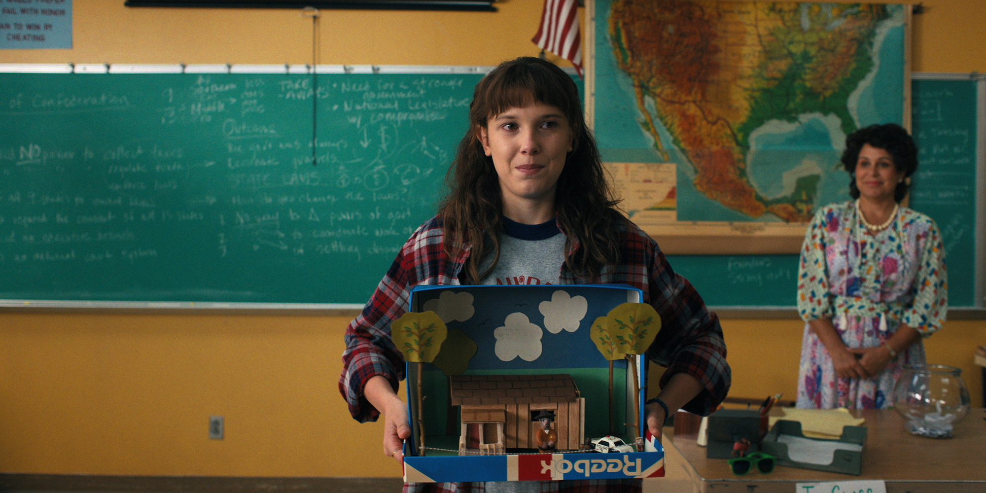 Millie Bobby Brown as Eleven holding a diorama in class in Stranger Things Season 4.