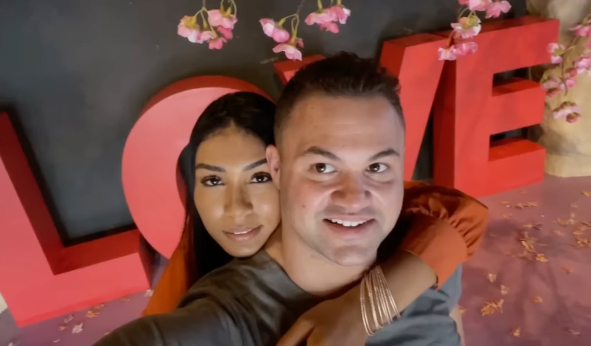 Thaís and Patrick hug each other in front of a big red sign that reads, 'Love' on '90 Day Fiancé' Season 9.