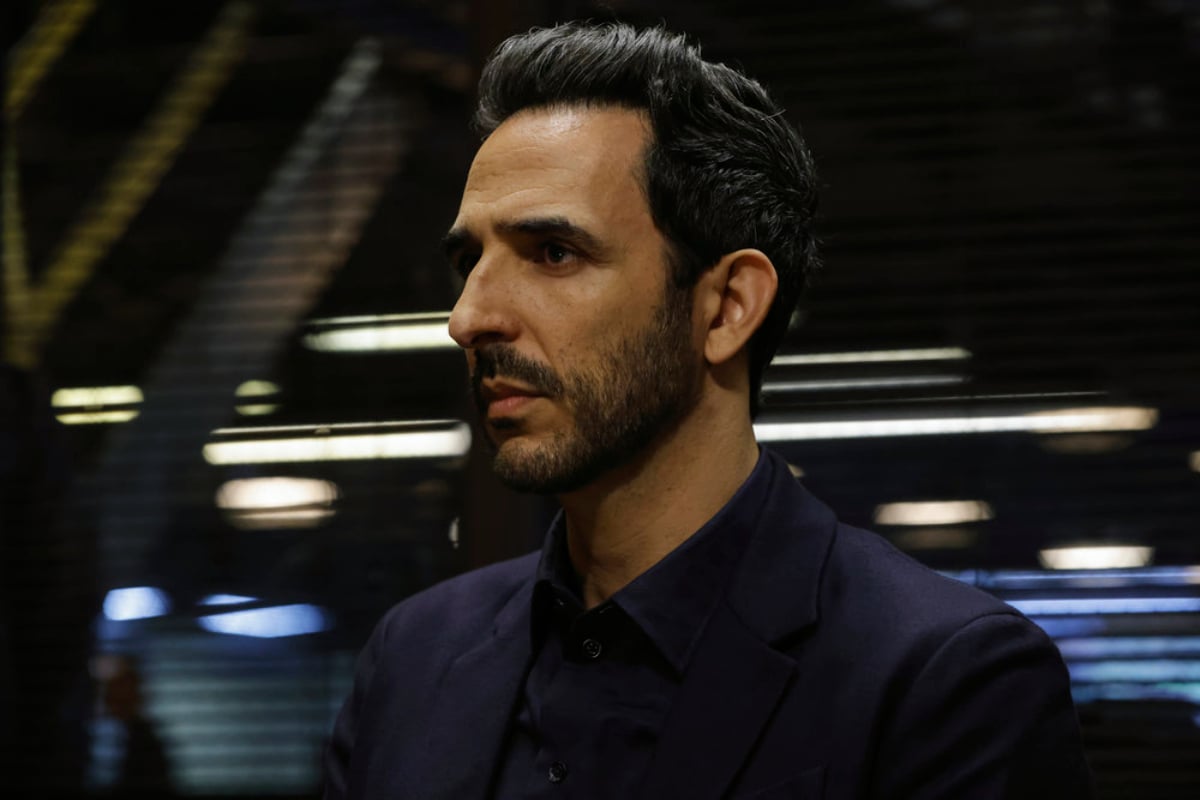 Amir Arison as Aram Mojtabai in The Blacklist Season 9. Aram wears a button-up shirt and looks serious. 