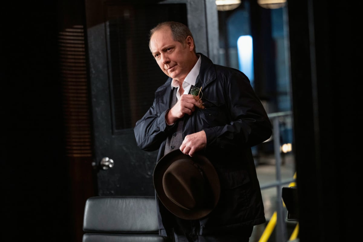 James Spader as Raymond Reddington in The Blacklist Season 9. Red puts his glasses in his pocket and holds his hat. 