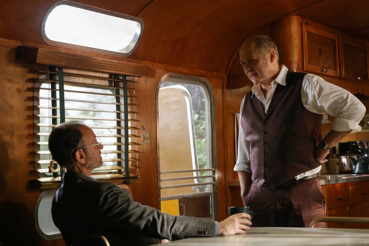 Fisher Stevens as Marvin Gerard and James Spader as Raymond Reddington in The Blacklist Season 9. Marvin sits at a table and faces Red who is standing. 