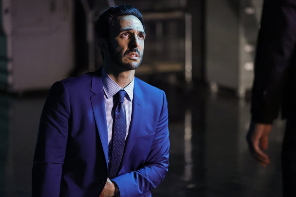 Amir Arison as Aram Mojtabai in The Blacklist Season 9. Aram kneels in front of someone wearing a blue suit.