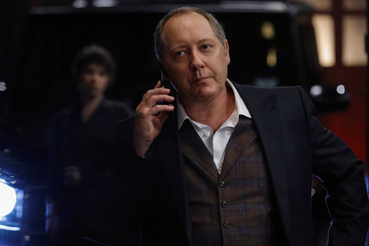 James Spader as Raymond Reddington in The Blacklist Season 9. Red holds a cellphone to his ear. Weecha can be seen behind him.