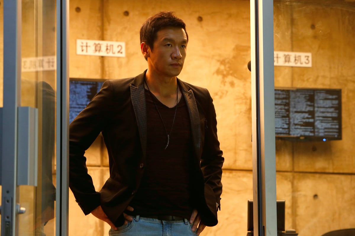 Chin Han returned as Wujing in The Blacklist Season 9 finale. Wujing wears a black shirt and jacket and jeans.
