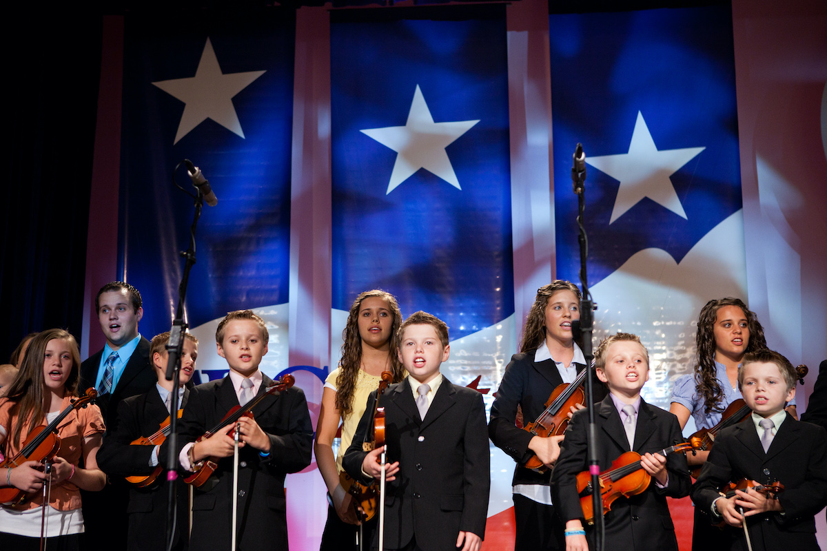 The Duggar family singing and performing in front of a blue and white background