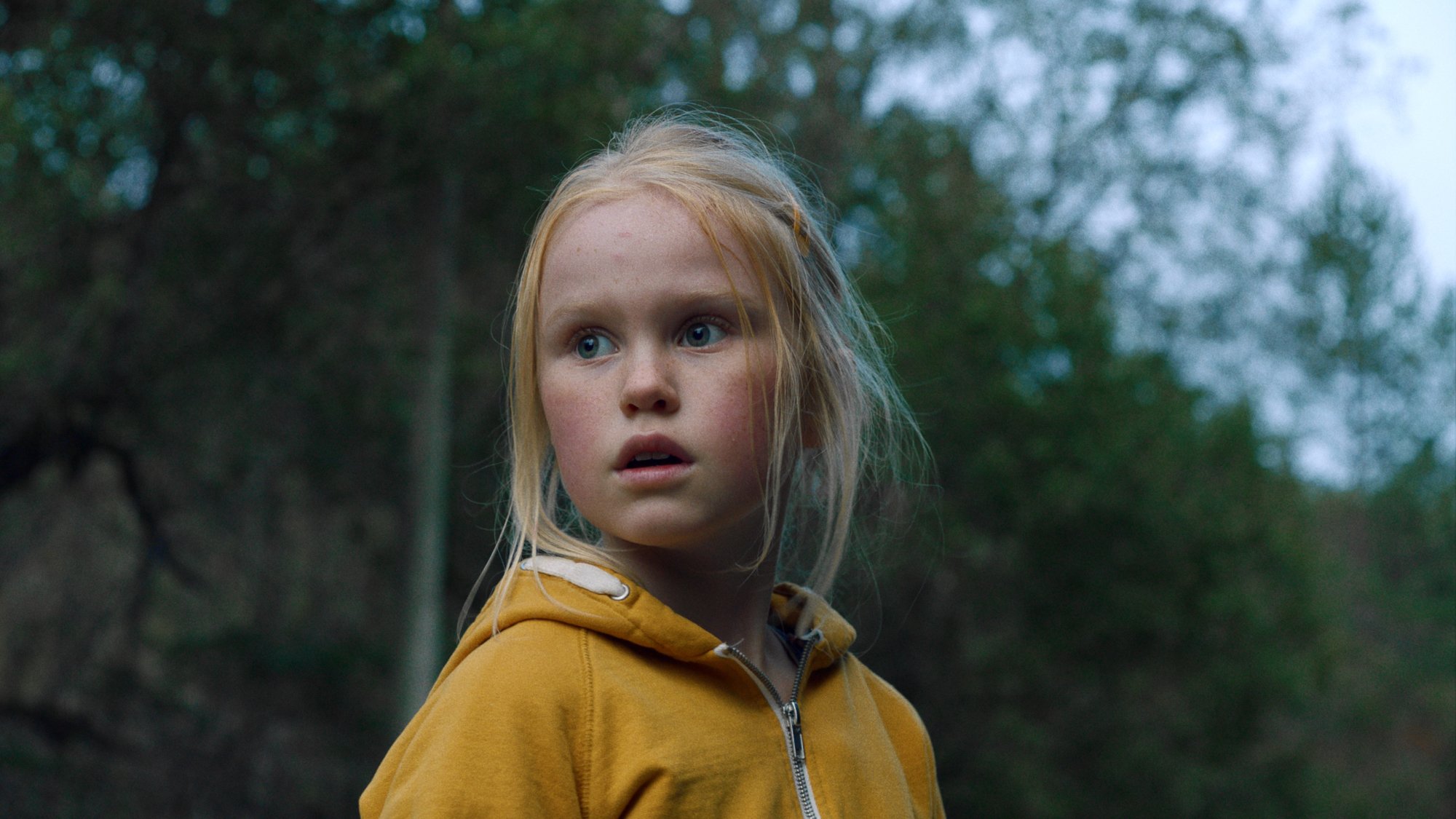 'The Innocents' Rakel Lenora Fløttum as Ida wearing a yellow jacket looking ahead with trees in the background
