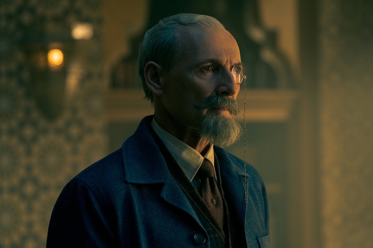 Close up of Sir Hargreeves standing in his living room wearing a suit and monocle in 'The Umbrella Academy'.