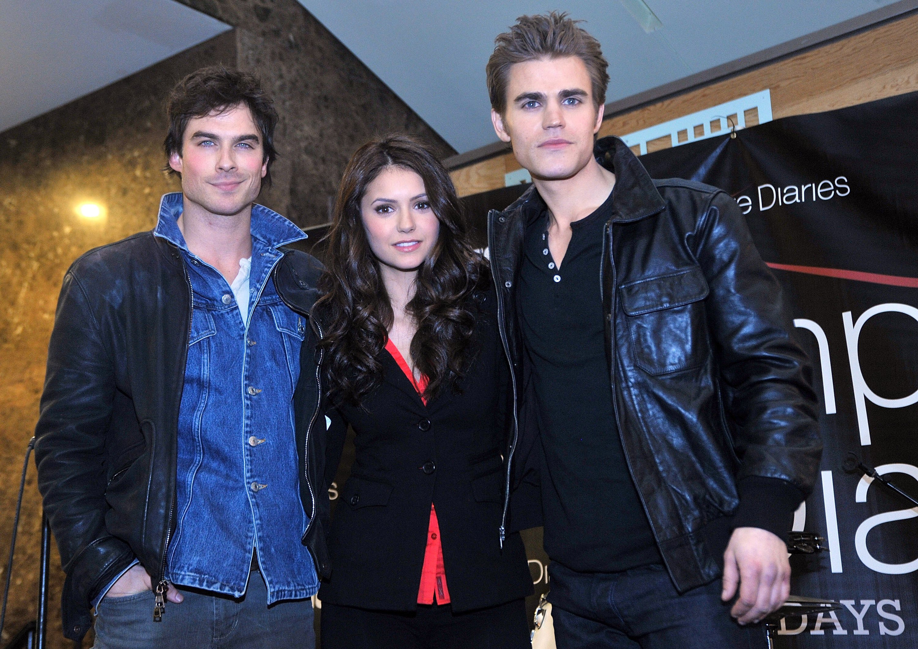 Ian Somerhalder, Nina Dobrev, and Paul Wesley, the cast of 'The Vampire Diaries,' which created two spinoffs, 'The Originals' and 'Legacies,' pose for a picture. Somerhalder wears a black leather jacket over a jean button-up shirt. Dobrev wears a black coat over a red shirt. Wesley wears a black leather jacket over a black shirt.