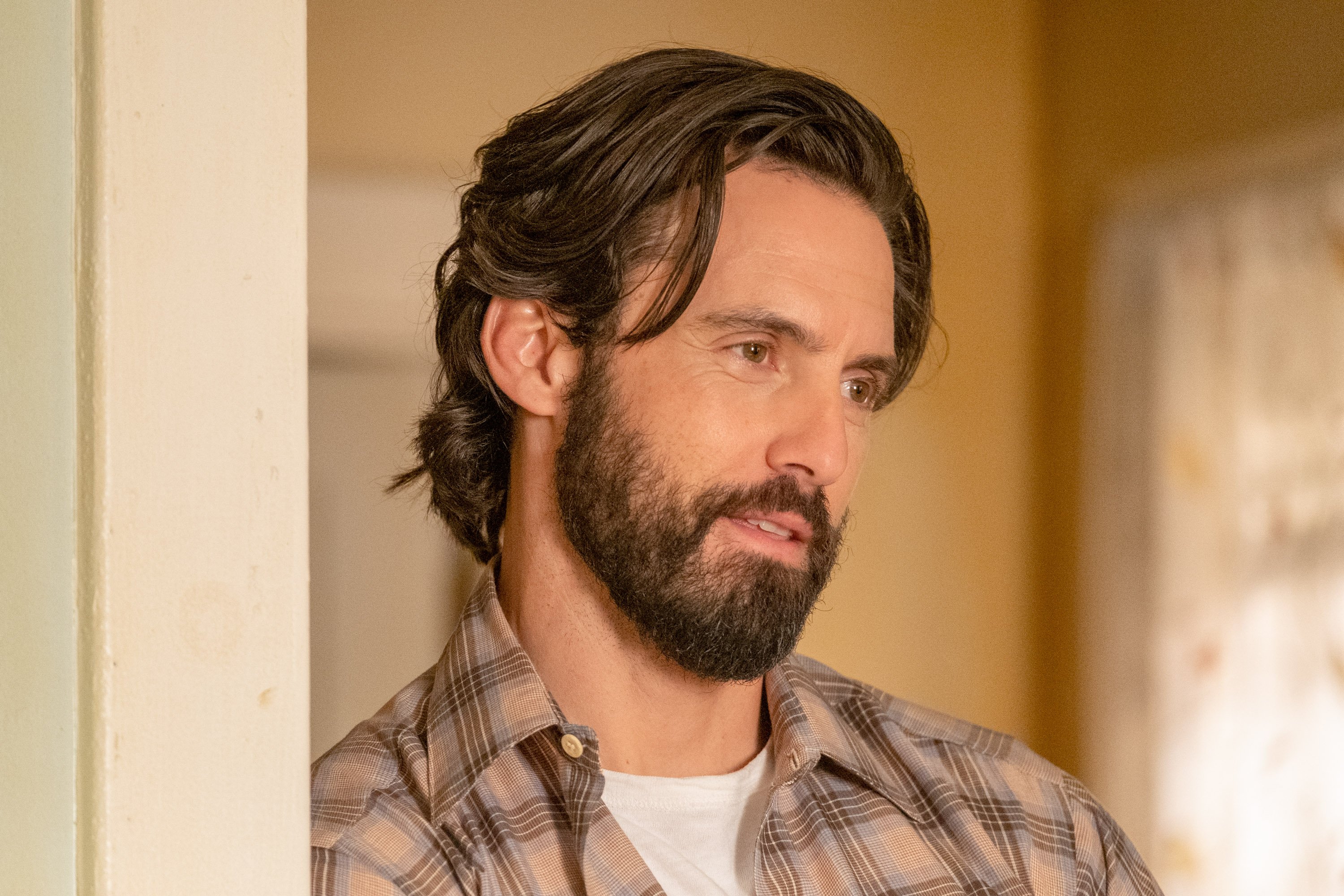 Milo Ventimiglia, in character as Jack Pearson in 'This Is Us' Season 6, wears a tan, brown, and blue plaid button-up shirt over a white shirt.