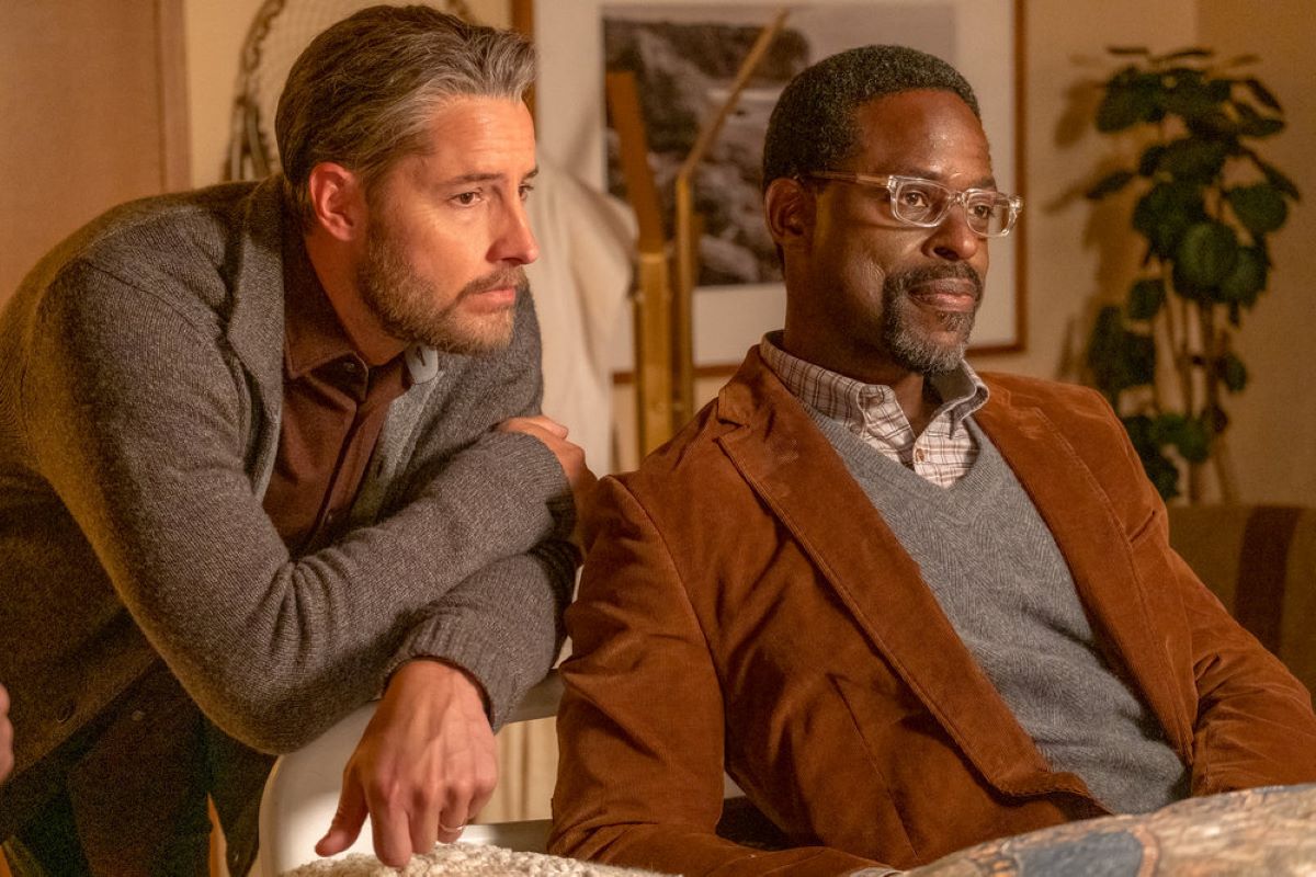 Justin Hartley and Sterling K. Brown, in character as Kevin and Randall in 'This Is Us' Season 6 Episode 17 on NBC, share a scene. Kevin wears a gray cardigan over a brown shirt. Randall wears a light brown suit over a gray sweater vest over a brown and white plaid shirt.