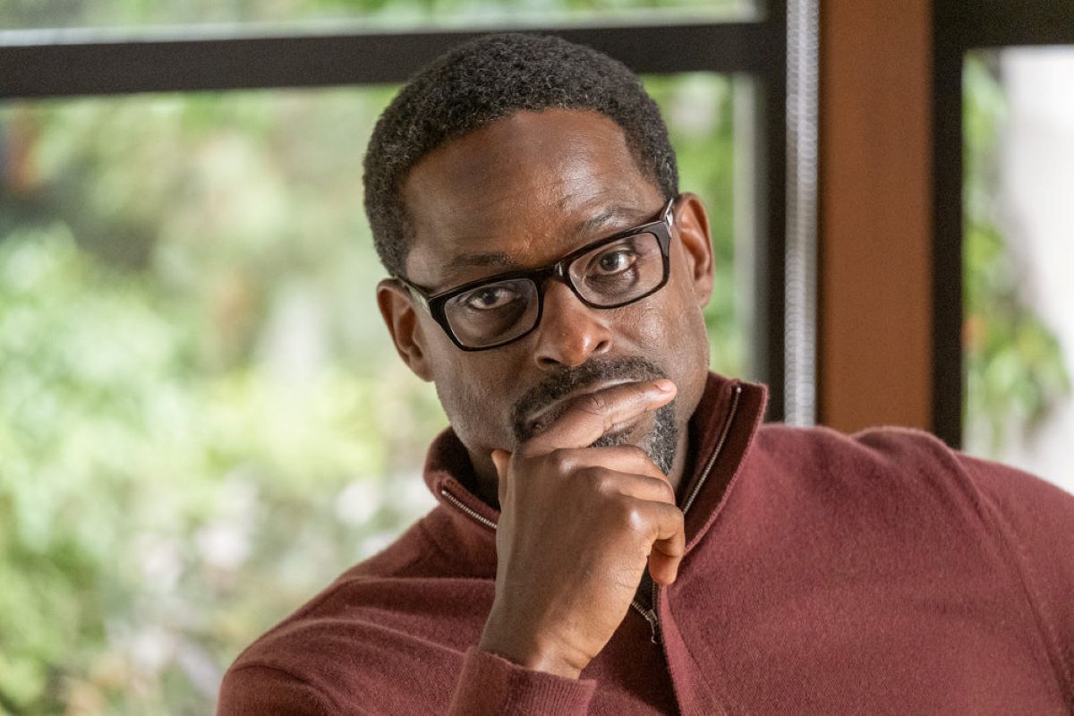 Sterling K. Brown, in character as Randall in 'This Is Us' Season 6 Episode 16, wears a dark red sweater and black-framed glasses.