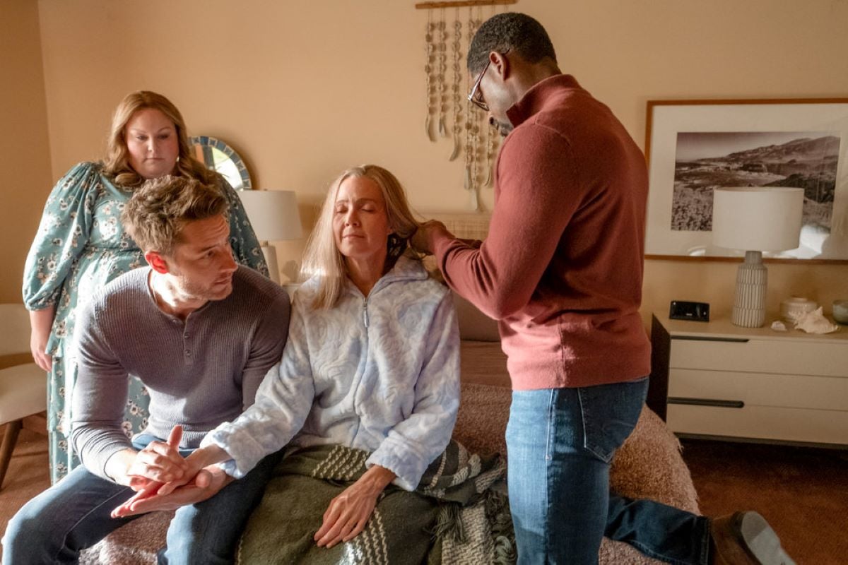 Chrissy Metz as Kate, Justin Hartley as Kevin, Mandy Moore as Rebecca, and Sterling K. Brown as Randall share a scene in 'This Is Us' Season 6 Episode 16. Kevin rubs lotion onto Rebecca's hands while Randall brushes her hair and Kate looks at them.