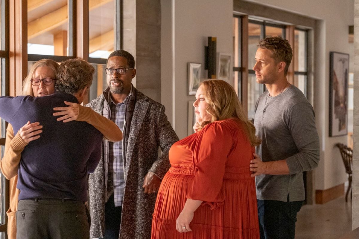 'This Is Us' Season 6 Episode 16 stars Jon Huertas as Miguel, Mandy Moore as Rebecca, Sterling K. Brown as Randall, Chrissy Metz as Kate, and Justin Hartley as Kevin share a scene. Miguel and Rebecca hug while the Big Three look at them concerned.