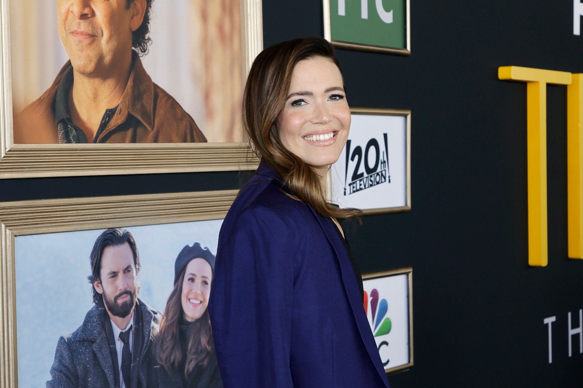 'This Is Us' star Mandy Moore, who says the penultimate episode felt like the series finale for her. She's wearing a blue blazer and standing in front of a wall with 'This Is Us' memorabilia on it.