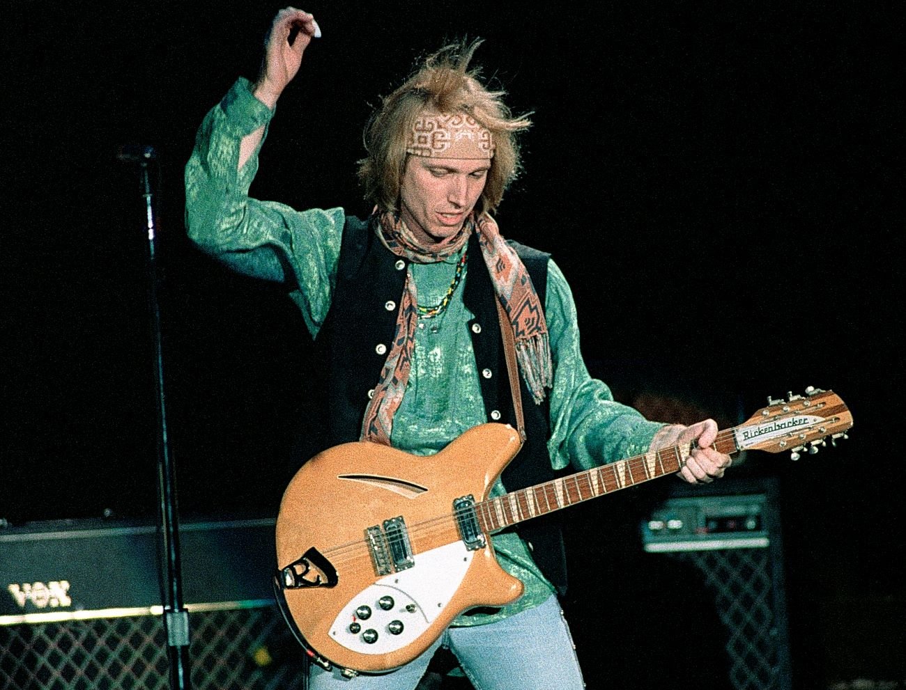 American musician Tom Petty wears a green shirt and vest and strums the guitar.