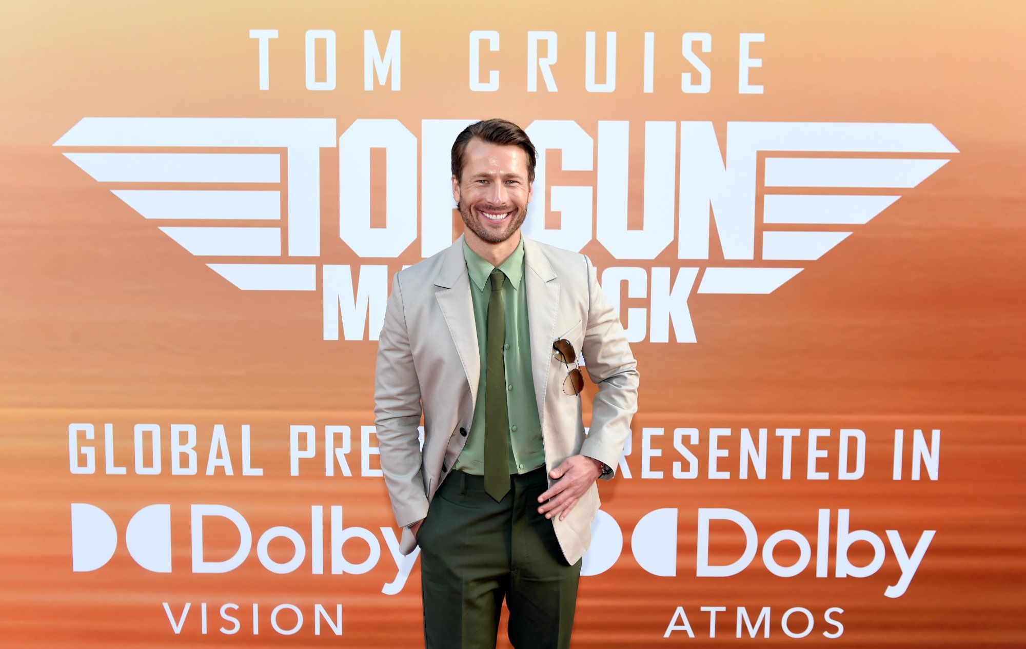 'Top Gun: Maverick' actor Glen Powell wearing a suit and smiling in front of the movie step and repeat