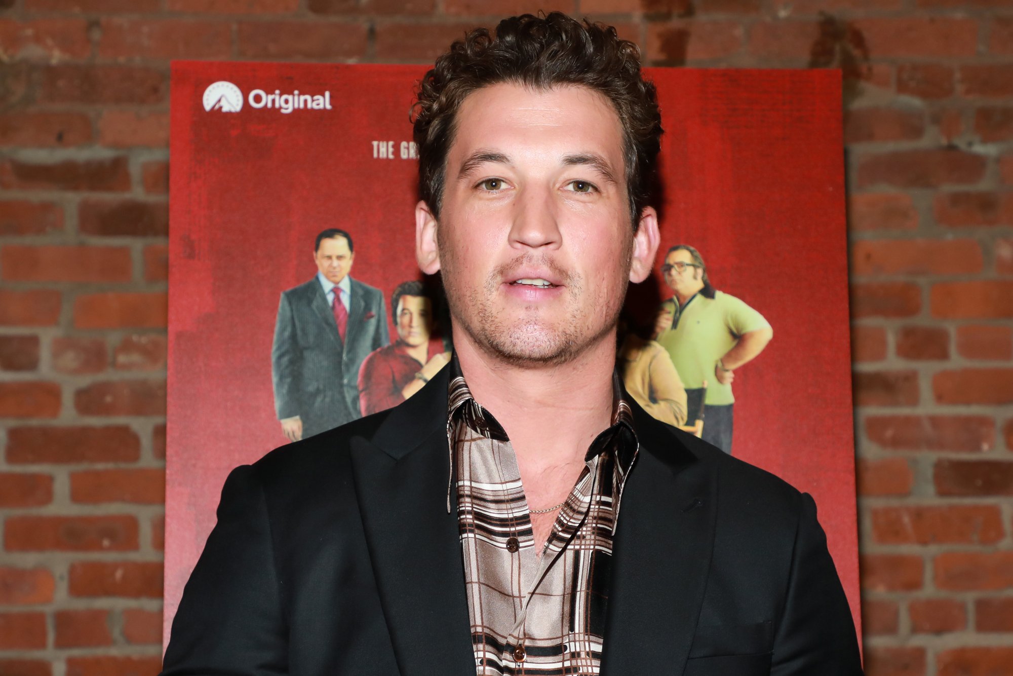 'Top Gun: Maverick' star Miles Teller wearing a suit in front of a poster and a brick wall