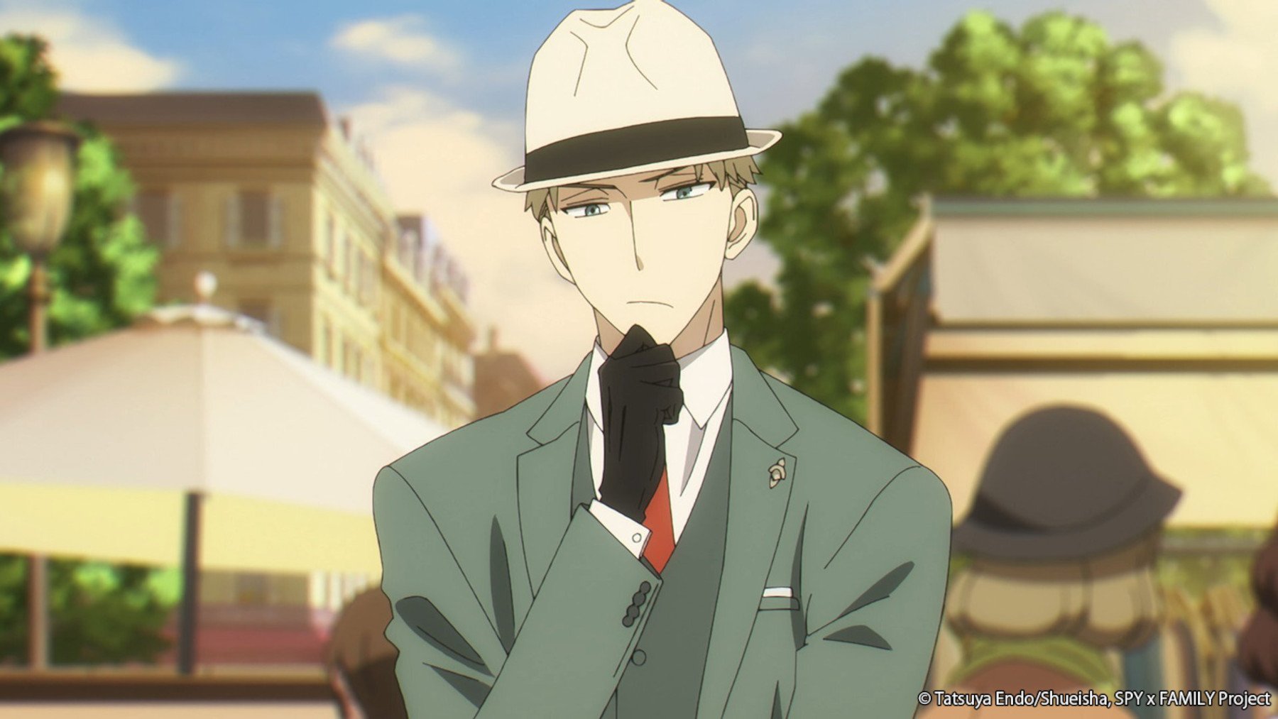 Twilight/Loid Forger in 'Spy x Family.' He's wearing a green suit, white hat, and black gloves. He's holding his chin and looks deep in thought.
