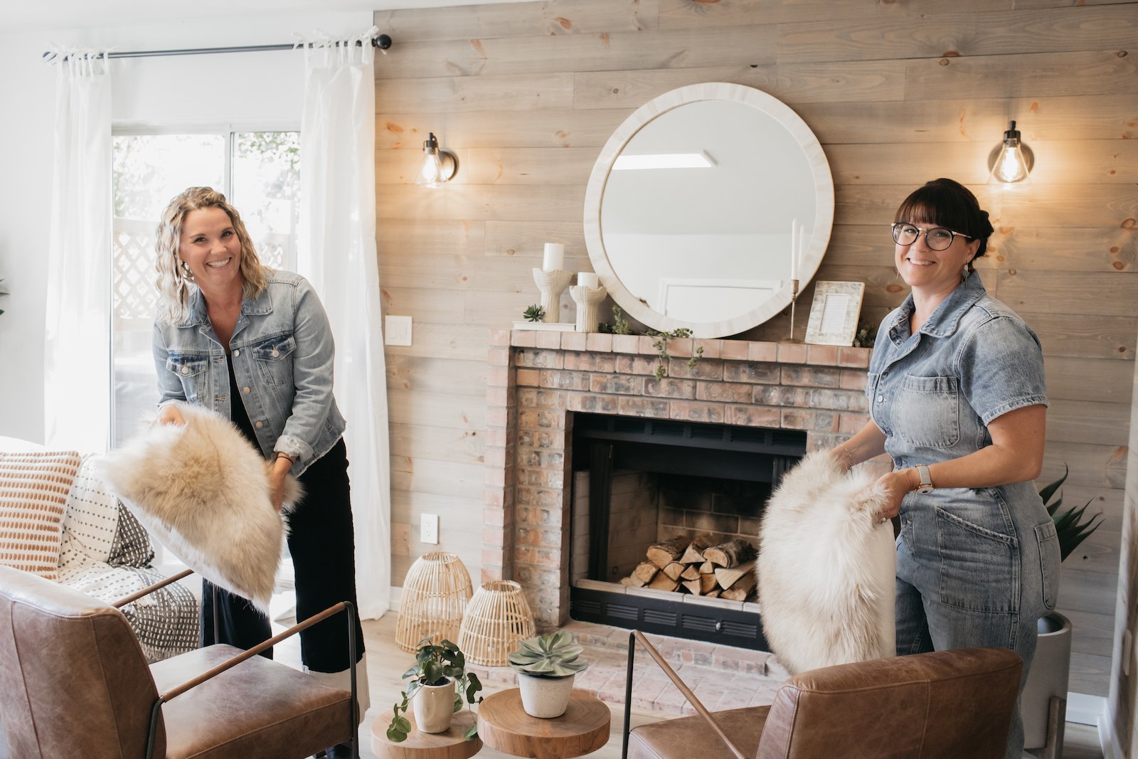 Leslie Davis & Lyndsay Lamb from 'Unsellable Houses' hold furry pillows and smile while staging a house 