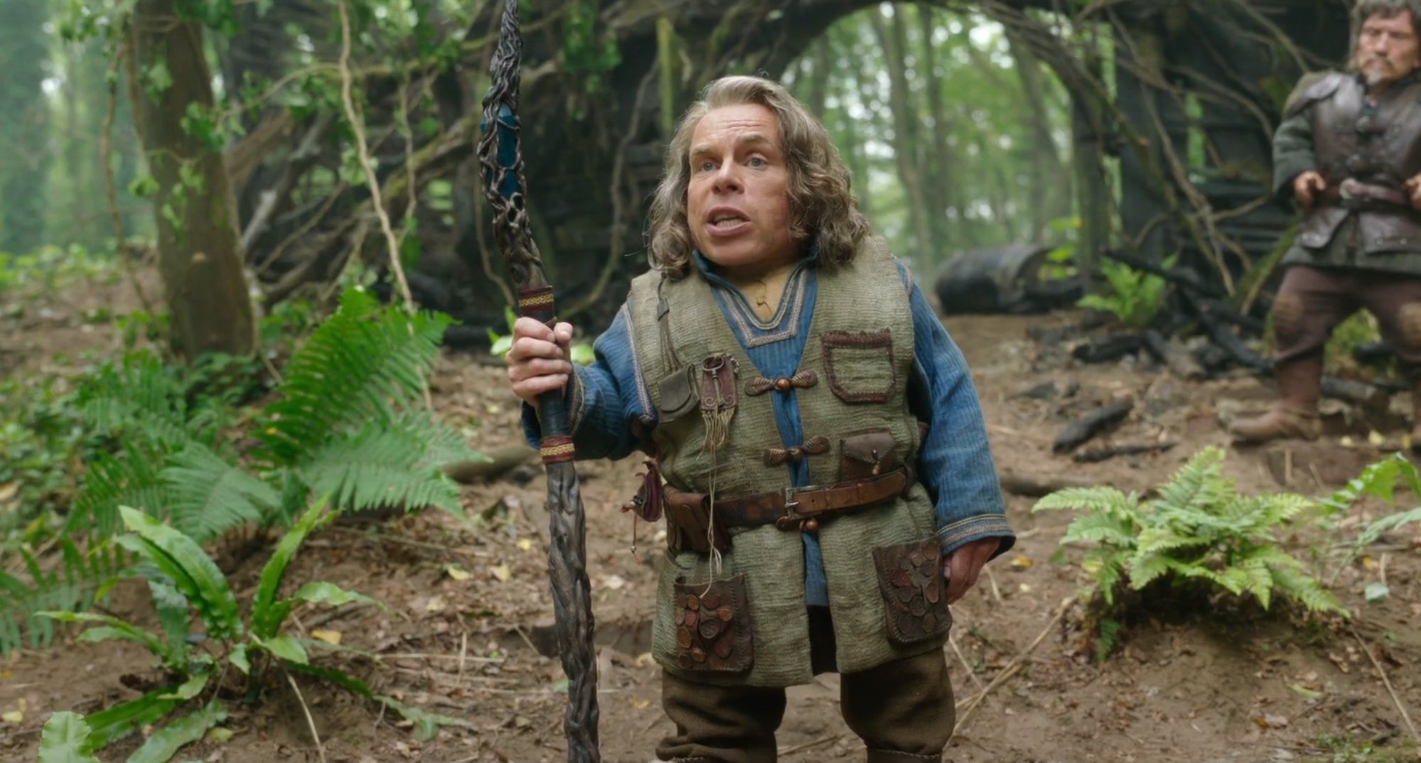 Warwick Davis as Willow Ufgood in the Disney+ series 'Willow' holding a staff in the forest.