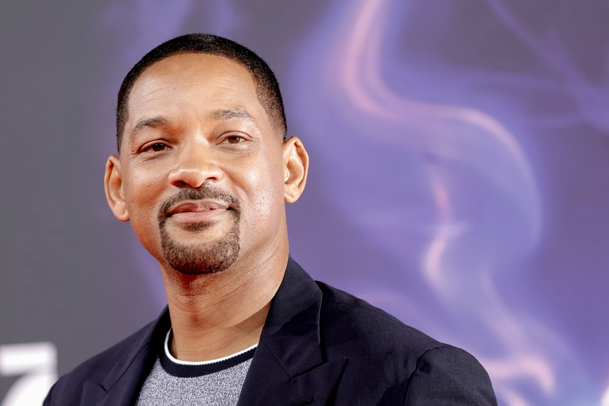 Will Smith smirking while wearing a grey shirt and a blazer.