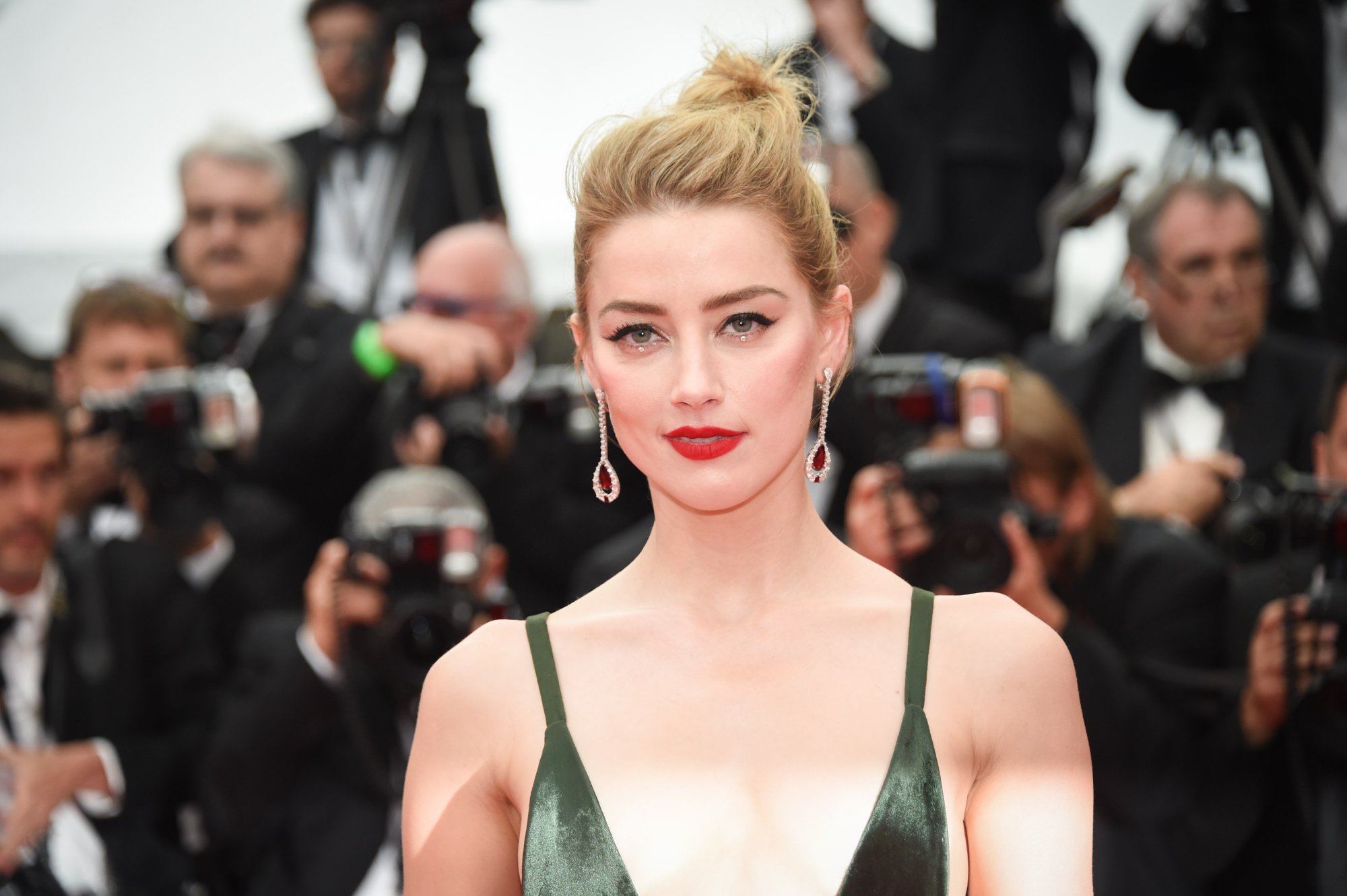'Zombieland' actor Amber Heard with a slight smile wearing a green dress in front of photographers wearing suits