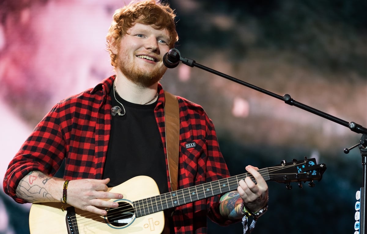 Ed Sheeran playing his guitar and seeing on stage.