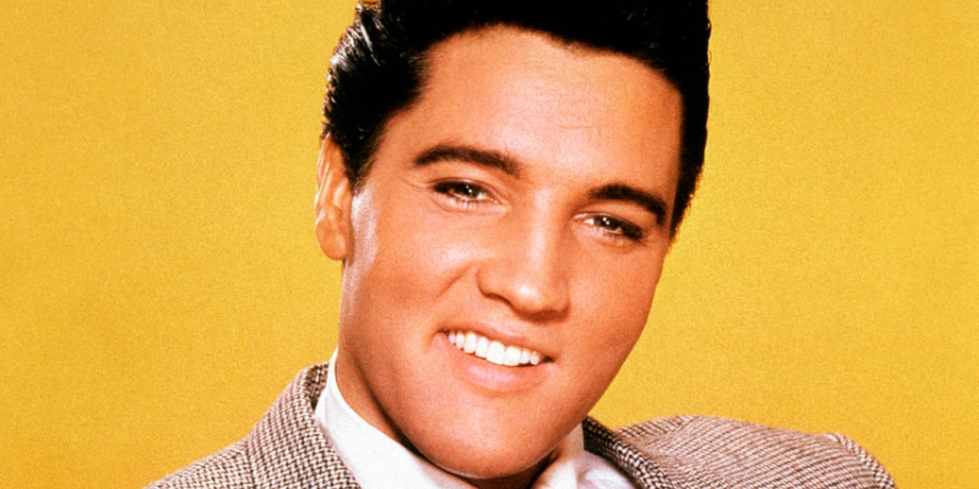 Elvis Presley in a press photograph with a bright yellow background.
