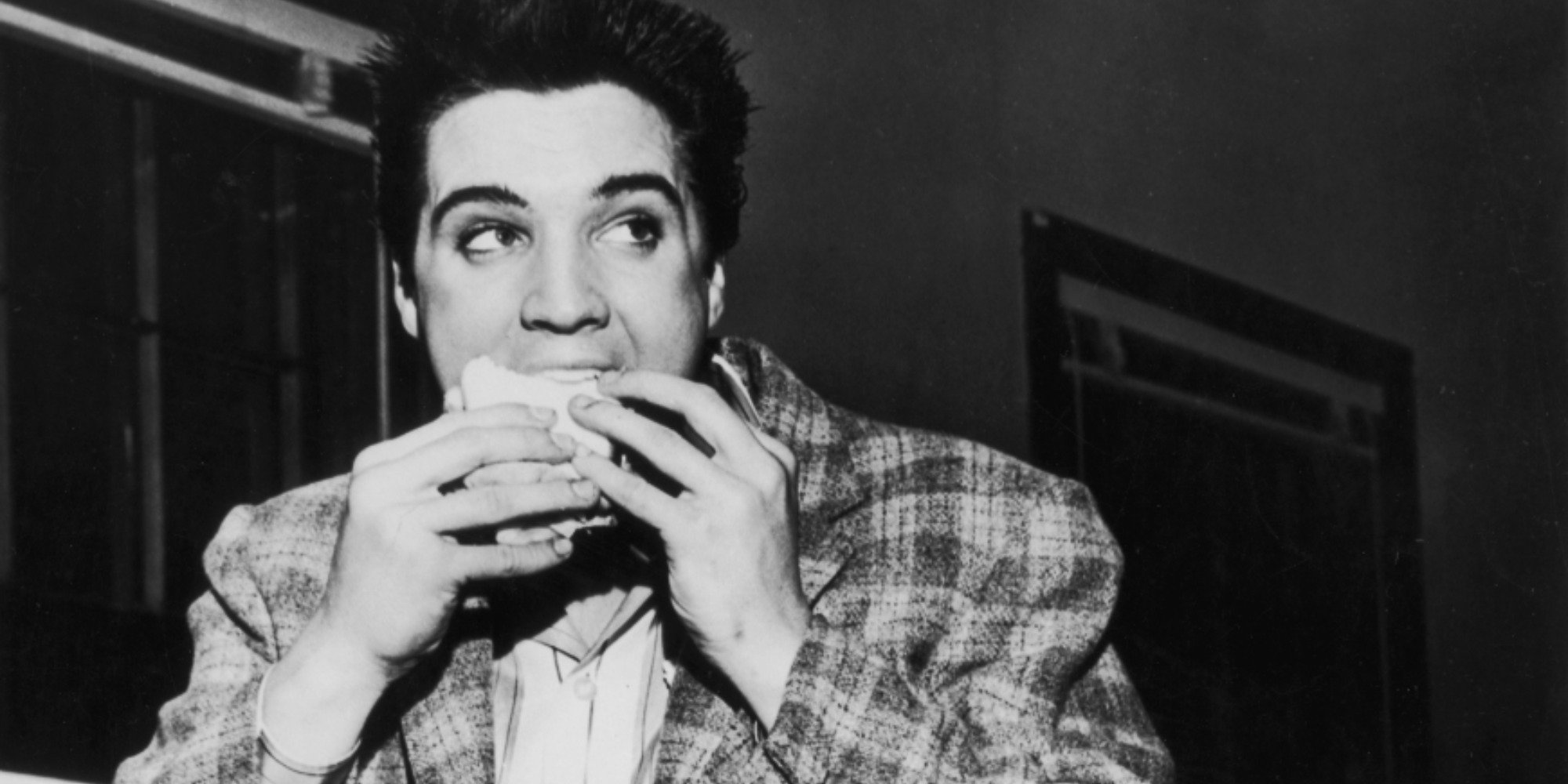 A black and white photo of Elvis Presley eating taken in 1958.