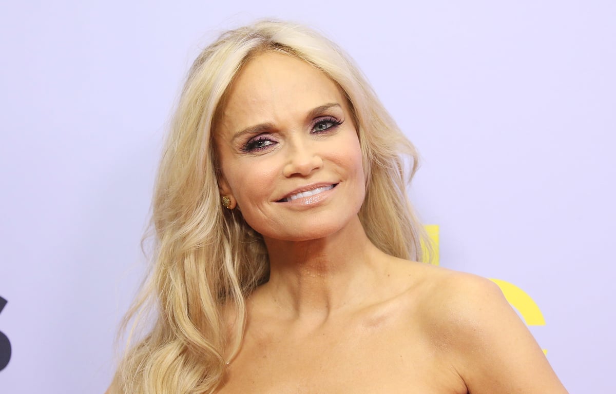 Kristin Chenoweth smiles in front of a purple backdrop.
