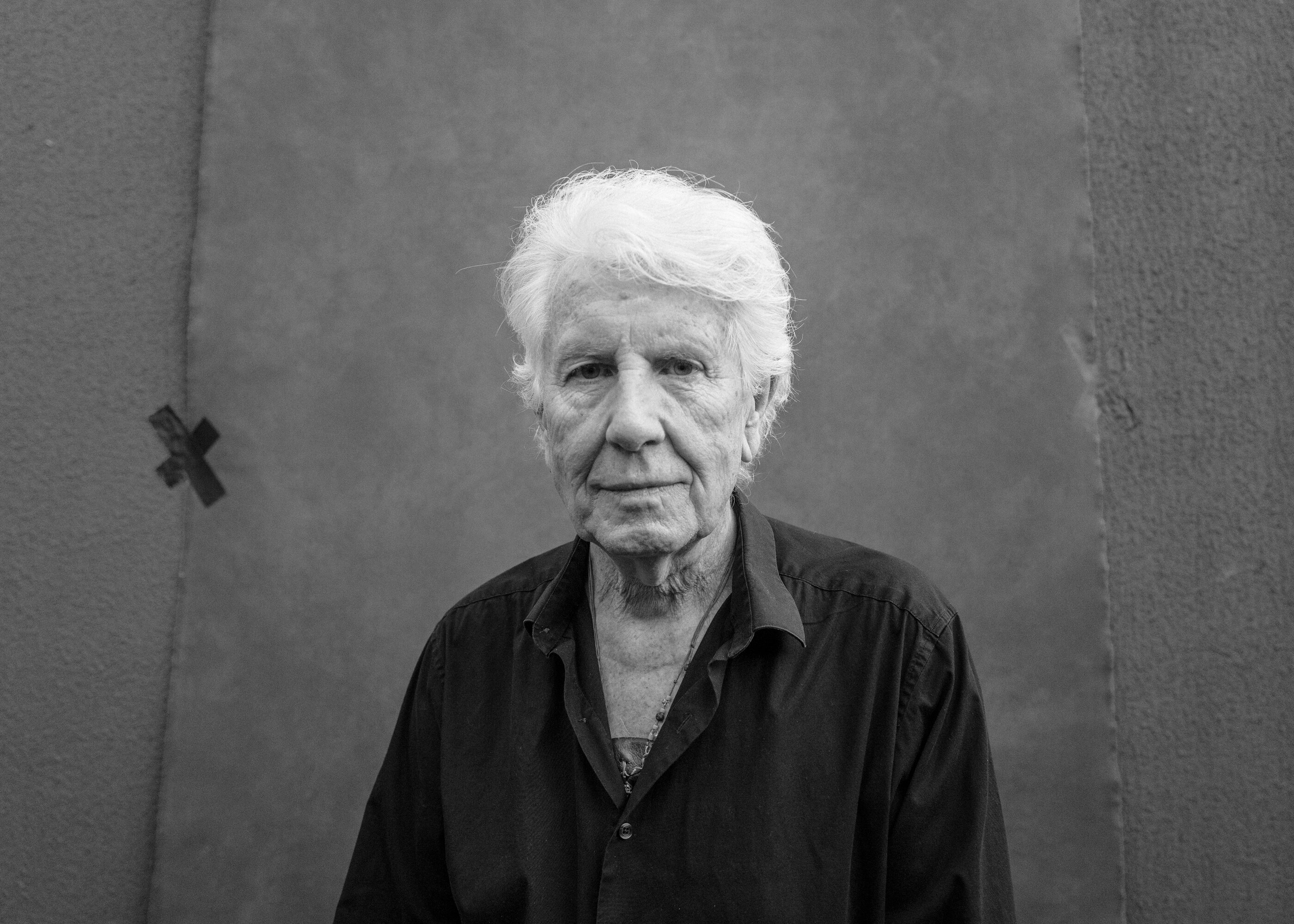 Graham Nash photographed in black and white against a wall.