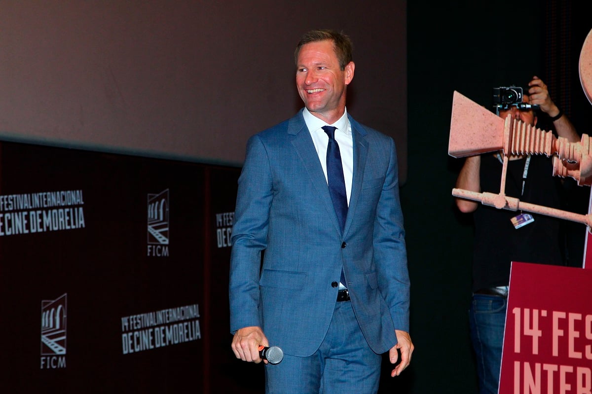 Aaron Eckhart smiling while wearing a blue suit.