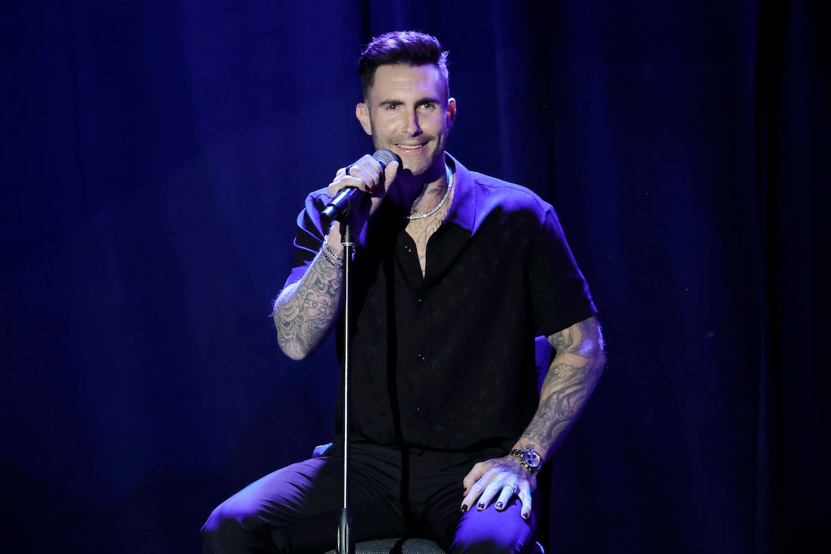 Adam Levine smiling, sitting behind a microphone